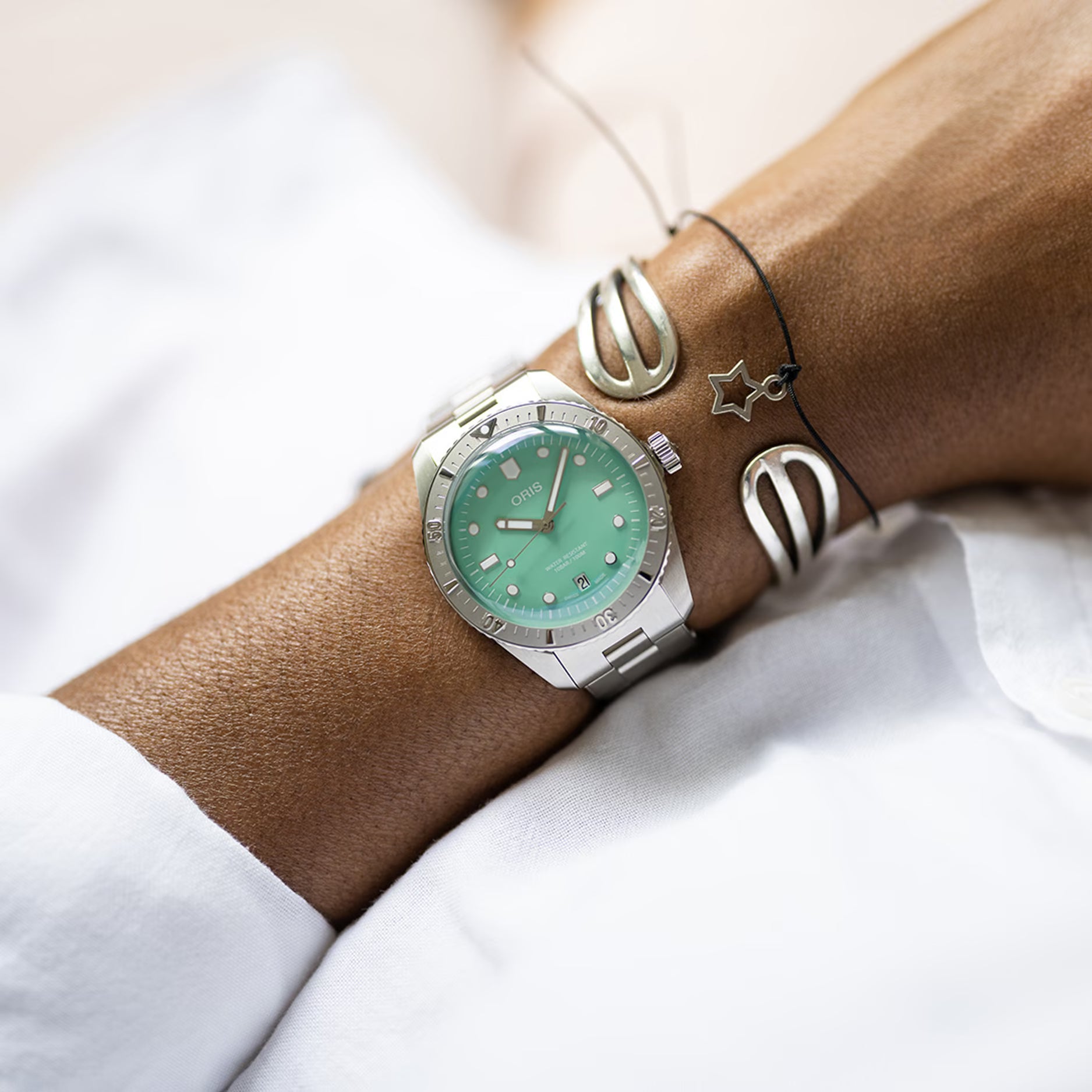 Oris Divers Sixty-Five Horloge 38mm met mintgroene wijzerplaat en roestvrijstalen band, gedragen om een pols met sieraden. Unisex Swiss Made horloge, ideaal voor dames en heren.