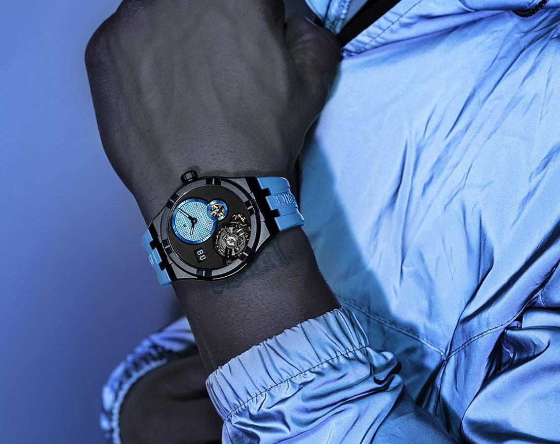 Maurice Lacroix Aikon klok 45mm kopen met blauw rubberen bandje en opengewerkte wijzerplaat, gedragen door man in blauwe jas.